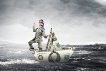 Businessman staying afloat on a paper boat made of a bank note