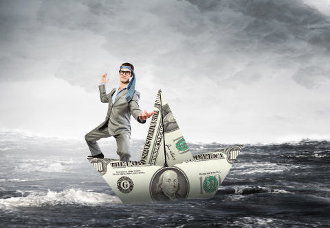 Businessman staying afloat on a paper boat made of a bank note